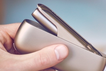 A gold IQOS device in its holder in a person's hand.