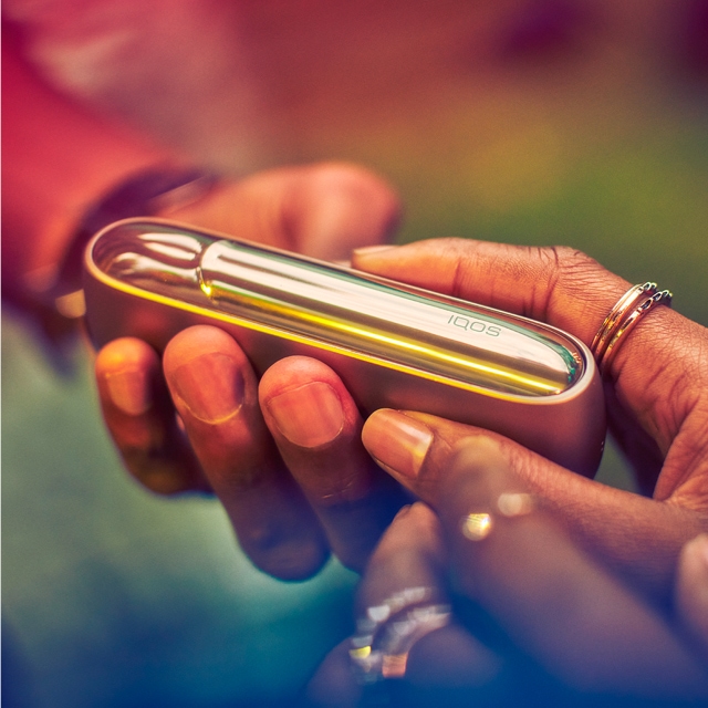 A person holding a brillliant gold IQOS device.