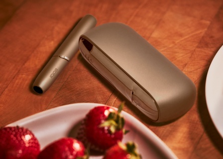 Brilliant gold IQOS 3 DUO holder and charger next to a plate of strawberries