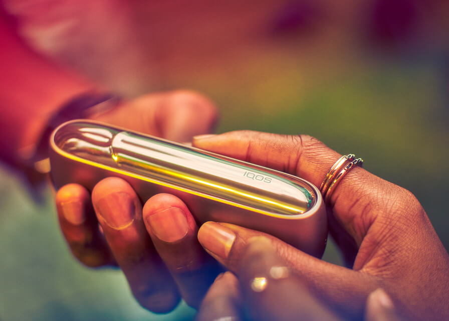 Close up of couple's hands passing along a brilliant gold IQOS 3 DUO device