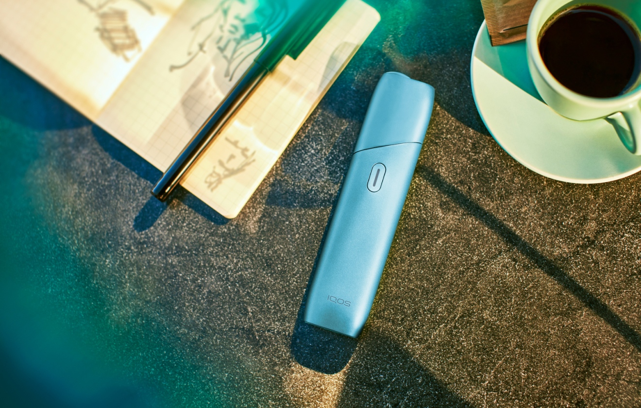 TurquoiseIQOS ORIGINALS ONE heated tobacco device on a table.
